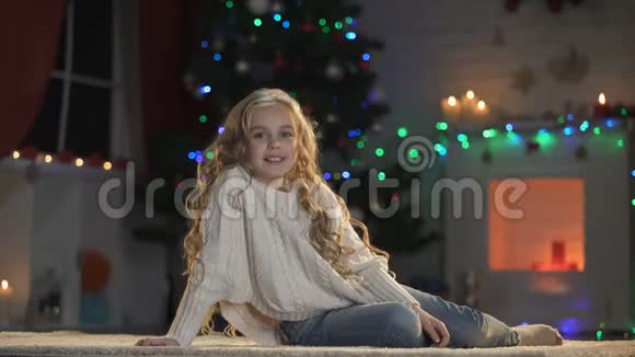 一个可爱的小女孩躺在装饰好的圣诞树下微笑着对着镜头视频的预览图