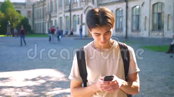 专心致志的亚洲男孩正在打电话一边想着回答一边站在靠近建筑物的路上阳光明媚视频的预览图