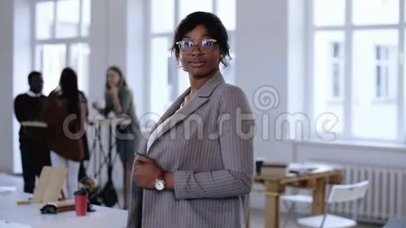 快乐职业年轻的黑人CEO商务女性穿着正式西装戴着眼镜摆姿势微笑着看着现代光办公室视频的预览图