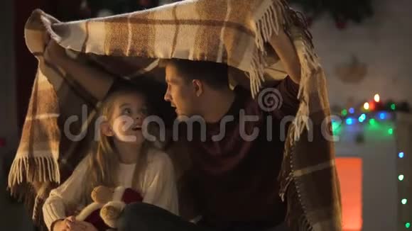 父亲为坐在舒适格子布下的小女孩讲述了令人叹为观止的圣诞故事视频的预览图