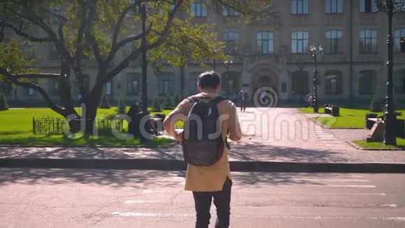 向后拍摄酷酷的亚洲男性在人行横道过马路向大学方向行进视频的预览图