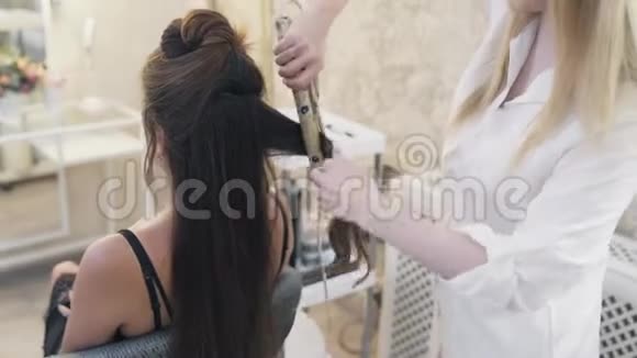 一个金色的理发师给一个留着深色长发的女孩剪发用一束头发视频的预览图