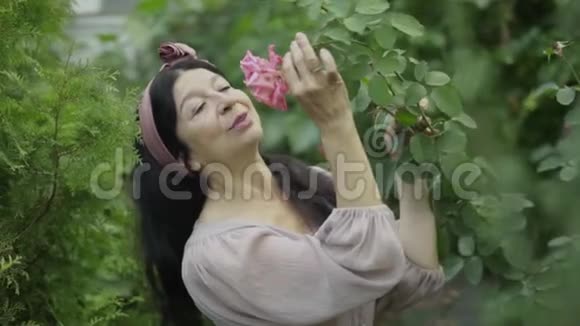 成熟的女人闻着花园里的玫瑰视频的预览图