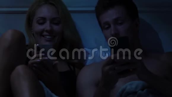 快乐的一对情侣在床上度过时光在智能手机上选择度假旅游视频的预览图