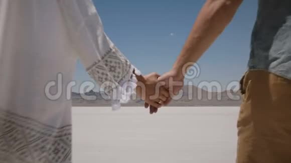 后景浪漫情侣牵着手走向犹他州盐沙漠中部的白色平地视频的预览图