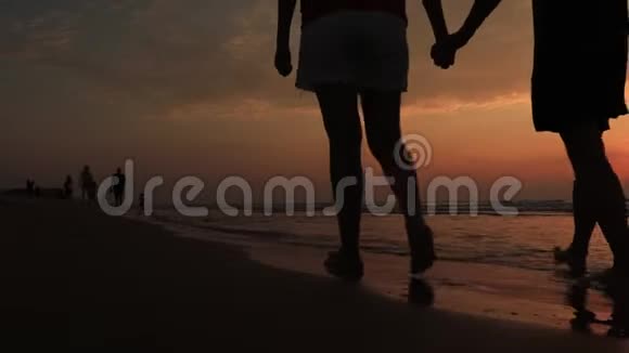 一对夫妇在海滩散步的剪影恋爱中的年轻夫妇在日落时分携手穿过海滩视频的预览图