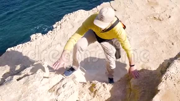一位穿着橙色毛衣的男性游客在海岸的背景下爬上了岩石表面散步度假活跃视频的预览图