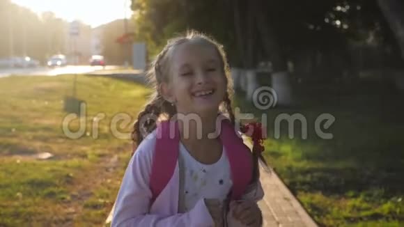 带背包的年轻女孩在阳光下快乐的微笑着带着辫子的青少年在耀斑的阳光下上学概念视频的预览图