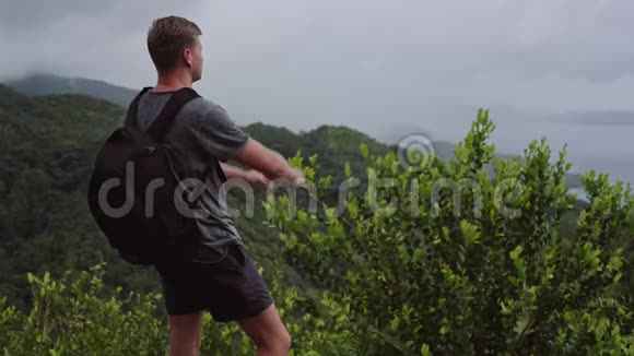 一个背着背包的旅行者站在山顶在他的手机上拍摄一幅风景视频的预览图