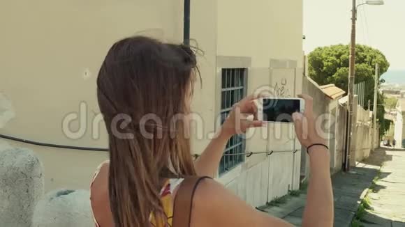年轻女子用智能手机拍摄地中海老街视频的预览图