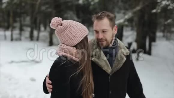 一对年轻迷人的夫妇在大雪下的冬林中散步和玩耍戴粉红帽子的男女拥抱视频的预览图