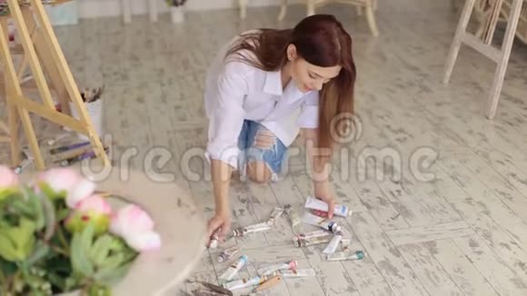 女孩艺术家从散落在地板上的地板上的油漆管中收集视频的预览图