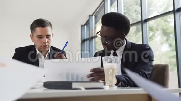 两个商人美国黑人和白种人穿着商务夹克坐在办公桌前讨论视频的预览图
