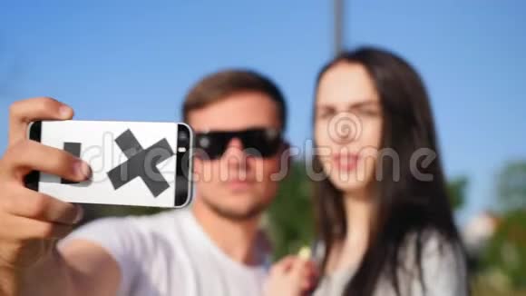 中镜头的快乐年轻夫妇自拍与智能手机同时站在公园附近的池塘近距离射击视频的预览图