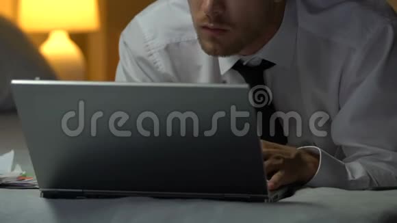 穿着商务西装的人在笔记本电脑上打字躺在酒店房间的床上出差视频的预览图