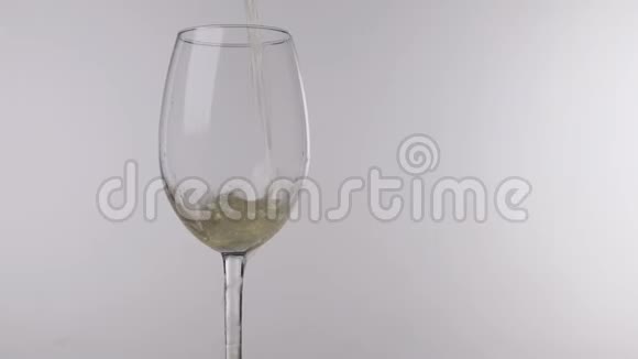 将白葡萄酒从瓶子中倒入白色背景上的玻璃杯中关闭视频的预览图