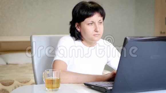 女孩博客坐在桌子旁用笔记本电脑喝茶视频的预览图