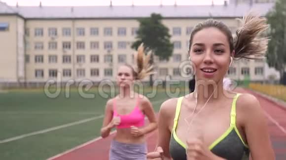 两个女孩穿着运动服在体育场周围奔跑的肖像健康的生活一个戴着耳机听音乐视频的预览图