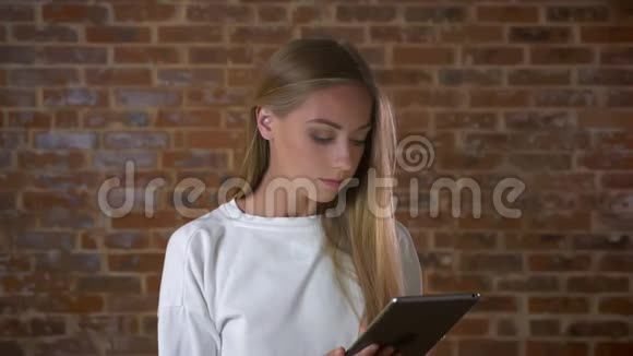 美丽的白种人女性正用专注的脸在平板电脑上滚动站在红色的屏幕上看着屏幕视频的预览图