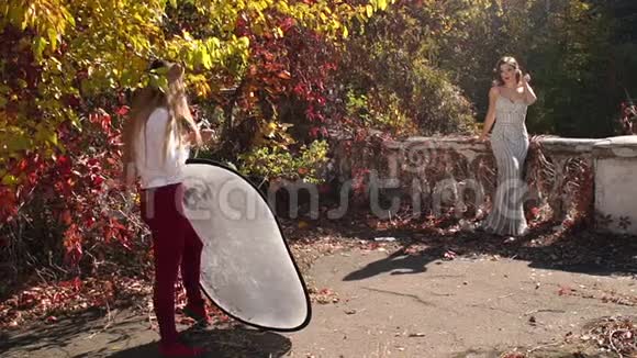 一位年轻的女摄影师在秋天公园给一个豪华的女孩模特拍照视频的预览图
