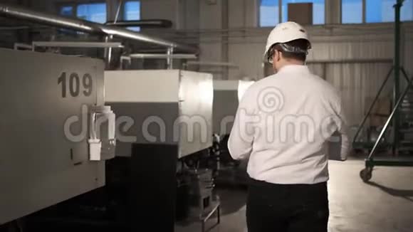戴着安全帽的工程师正带着平板电脑穿过一家重工业工厂慢动作背面视图视频的预览图