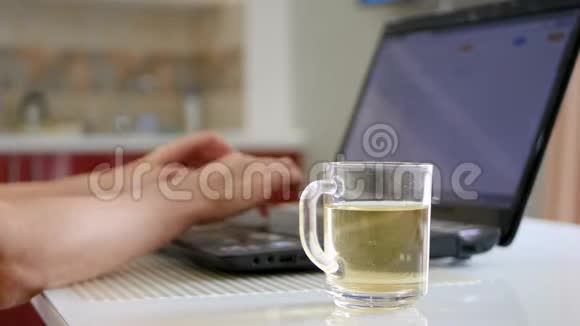 女孩的手在笔记本电脑键盘上打字旁边的笔记本电脑一杯茶女孩的手拿着一杯茶视频的预览图