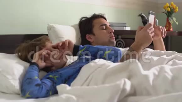 两个穿着睡衣的可爱兄弟早上躺在卧室的床上哥哥正在用手机发短信视频的预览图