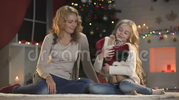 快乐的女儿和妈妈坐在圣诞树附近拥抱和等待着假期视频的预览图