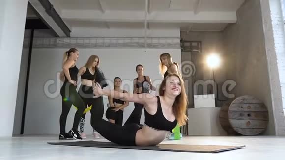 年轻的微笑的女人热身拱起伸展着背抱着腿在瑜伽课上锻炼视频的预览图