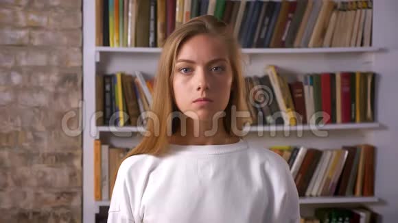 严肃专注的脸漂亮的白种人女孩看着砖头工作室书架上的书旁边的相机视频的预览图