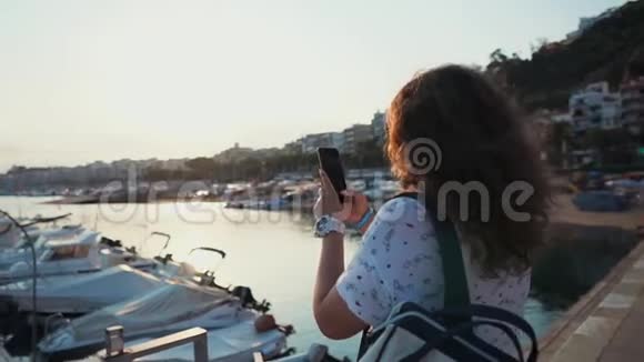 女子正在城市港口用移动摄像机拍摄停泊的游艇视频的预览图