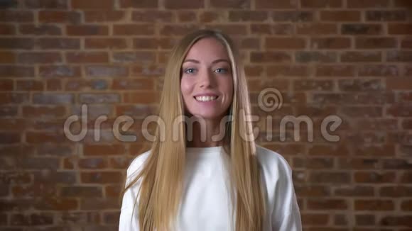 一个美丽的白人女孩站在砖砌的工作室里笔直地对着镜头微笑魅力四射视频的预览图