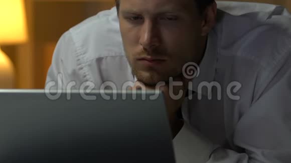 疲倦的人打哈欠在笔记本电脑上看报告躺在床上过度劳累的人视频的预览图
