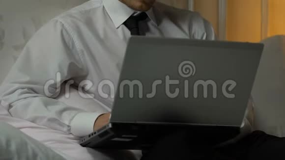 疲惫的男性晚上在笔记本电脑上工作坐在酒店房间里出差视频的预览图