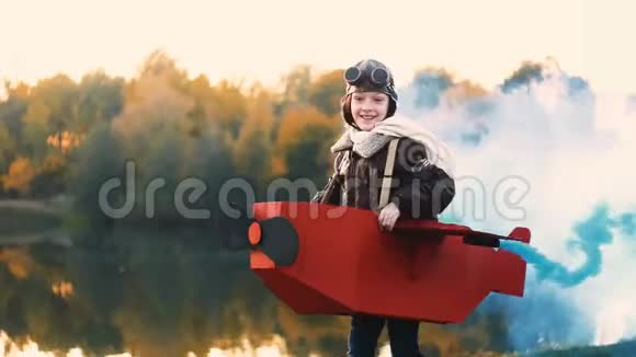 小飞行员女孩跑在日落湖在有趣的纸板飞机与蓝色烟雾玩飞行员慢动作视频的预览图