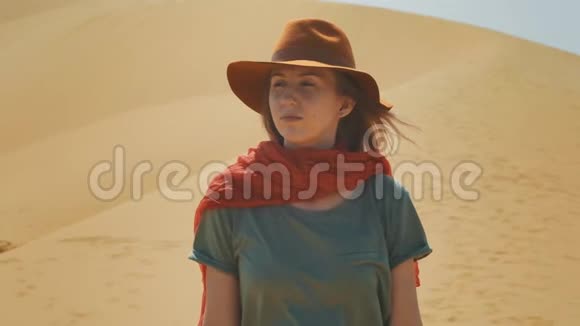 肖像沙漠中的女孩旅行者在沙滩上戴着帽子和红领巾探索古老的地形寻找视频的预览图