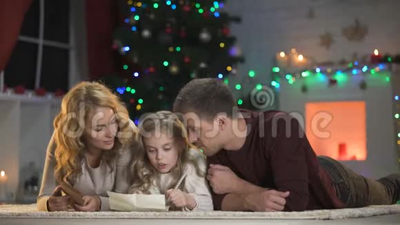 女孩把给圣诞老人的信放进信封里和父母躺在圣诞树下视频的预览图