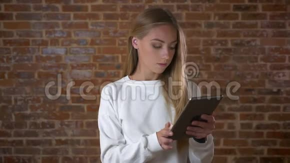 超棒的白种人女孩在平板电脑上打字注意力很集中站在靠近砖块的红色工作室的镜头旁边视频的预览图