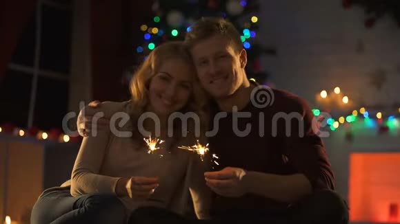 有孟加拉灯的情侣坐在装饰好的圣诞树附近的舒适房间里视频的预览图