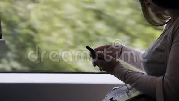 一个夏天美丽的女孩坐在城市的通勤列车上在智能手机上输入短信视频的预览图