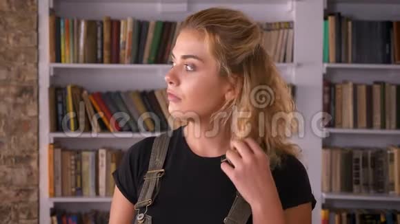 自信善良的白种人女人摸着她卷曲的红色头发看着图书馆里的摄像机视频的预览图