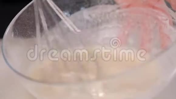 一位女厨师糕点厨师用金属搅拌器在玻璃碗里搅拌面团视频的预览图