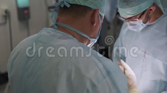 两名医生在手术期间穿着无菌衣服和口罩手术室的外科医生背面视图视频的预览图