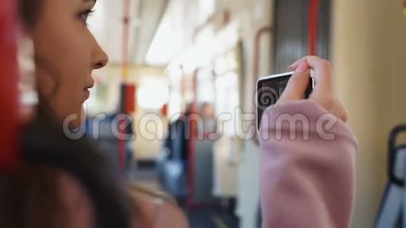 女孩在乘公共汽车旅行时用电话拍摄城市现场直播旅行博客视频的预览图