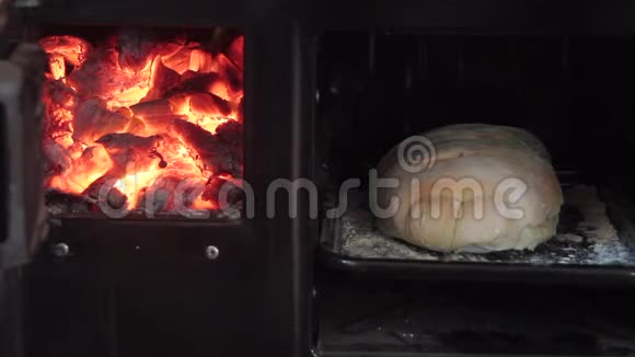 手从燃木的烤箱里拿了一个刚出炉的面包旁边放着火和闪闪发光的余烬视频的预览图