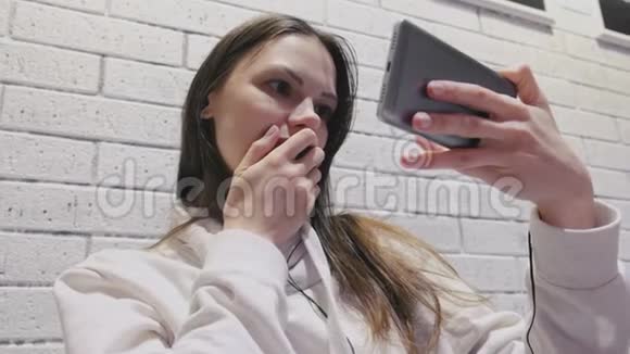 一位美丽的黑发女人在砖墙上戴着耳机看着令人惊叹的塞尔维亚语视频的预览图