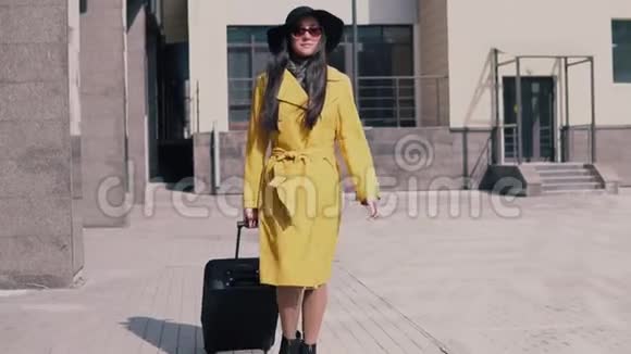 穿着黄色雨衣帽和带行李的眼镜的时髦女孩坐出租车视频的预览图
