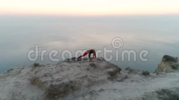 美丽的运动女性正在做瑜伽伸展在山顶与海景在日落空中镜头视频的预览图