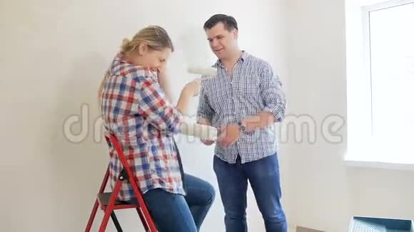 幸福的年轻夫妇在他们的新房子里装修时玩得很开心用油漆滚筒互相打着视频的预览图