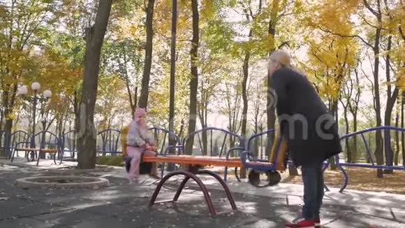 小女孩和她的母亲骑着秋千在秋天的城市公园视频的预览图